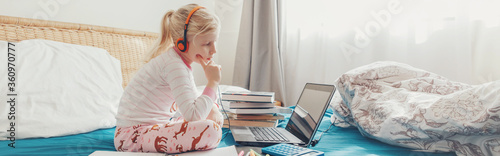 Girl child sitting in bed and learning online on laptop Internet. Virtual class lesson on video during self isolation quarantine. Distant remote education class. Web banner header for a website.