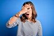 © Krakenimages.com - Young beautiful blonde girl wearing casual sweater standing over blue isolated background peeking in shock covering face and eyes with hand, looking through fingers with embarrassed expression.