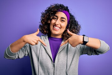 Wall Mural - Beautiful curly arab sportswoman doing sport wearing sportswear over purple background looking confident with smile on face, pointing oneself with fingers proud and happy.