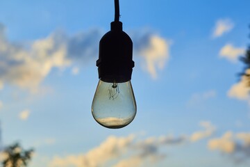 Poster - Closeup shot of a light bulb with the cloudy evening sky in the background