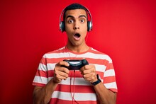 Handsome African American Gamer Man Playing Video Game Using Jostick And Headphones Scared In Shock With A Surprise Face, Afraid And Excited With Fear Expression
