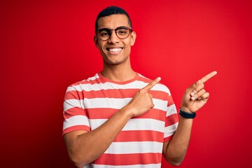 Wall Mural - Young handsome african american man wearing casual striped t-shirt and glasses smiling and looking at the camera pointing with two hands and fingers to the side.