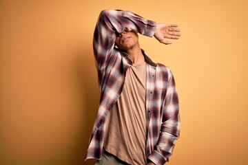Wall Mural - Young handsome african american man wearing casual shirt standing over yellow background covering eyes with arm, looking serious and sad. Sightless, hiding and rejection concept