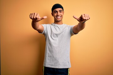 Wall Mural - Handsome african american sportsman doing sport wearing sportswear over yellow background approving doing positive gesture with hand, thumbs up smiling and happy for success. Winner gesture.