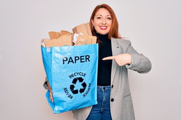 Poster - Young beautiful redhead woman recycling holding paper bag with cardboard to recycle very happy pointing with hand and finger