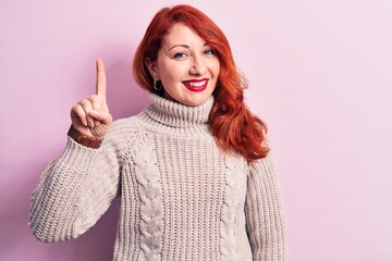 Poster - Young beautiful redhead woman wearing casual turtleneck sweater over pink background smiling with an idea or question pointing finger up with happy face, number one