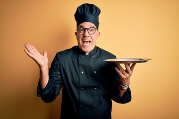 Sticker - Middle age handsome grey-haired waiter man wearing cooker uniform and hat holding tray very happy and excited, winner expression celebrating victory screaming with big smile and raised hands