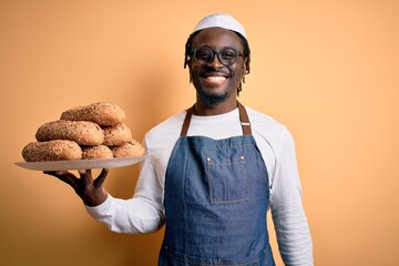 Young african american bakery man holding tray with healthy wholemeal bread with a happy face standing and smiling with a confident smile showing teeth