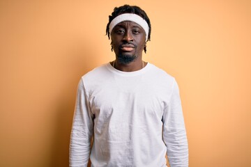 Sticker - Young african american man doing sport wearing sportswer over isolated yellow background with serious expression on face. Simple and natural looking at the camera.