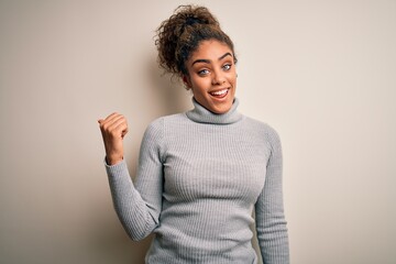 Sticker - Beautiful african american girl wearing turtleneck sweater standing over white background smiling with happy face looking and pointing to the side with thumb up.