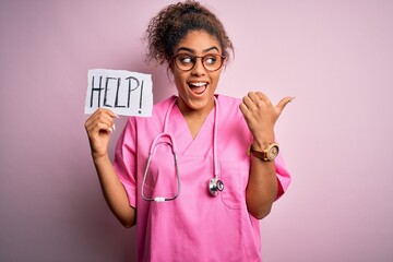 Canvas Print - African american doctor girl wearing medical uniform and stethoscope holding help paper pointing and showing with thumb up to the side with happy face smiling