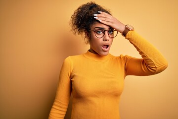 Poster - Young beautiful african american girl wearing sweater and glasses over yellow background surprised with hand on head for mistake, remember error. Forgot, bad memory concept.