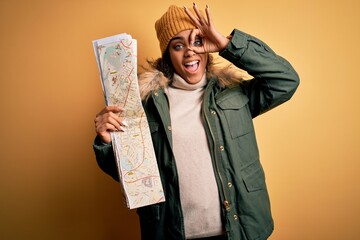 Wall Mural - African american skier tourist girl wearing snow sportswear and ski goggles holding city map with happy face smiling doing ok sign with hand on eye looking through fingers