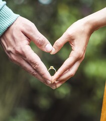 Sticker - Vertical shot of a heart of hands by a couple holding an engagement ring on a greenery background