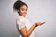 © Krakenimages.com - Young beautiful african american girl wearing casual t-shirt standing over white background pointing aside with hands open palms showing copy space, presenting advertisement smiling excited happy