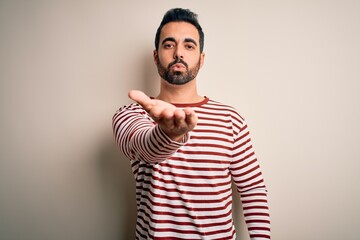 Poster - Young handsome man with beard wearing casual striped t-shirt standing over white background looking at the camera blowing a kiss with hand on air being lovely and sexy. Love expression.