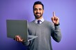 © Krakenimages.com - Young handsome businessman with beard working using laptop over purple background surprised with an idea or question pointing finger with happy face, number one