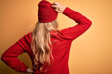 Poster - Young beautiful blonde woman wearing casual sweater and wool cap over white background Backwards thinking about doubt with hand on head