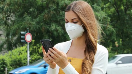 Wall Mural - Young beautiful woman with protective mask using smart phone app in city street with traffic cars on the background