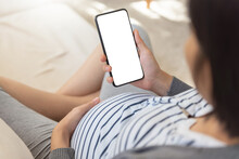 Asian Pregnant Woman Using Smartphone And Doing Online Shopping On Sofa.