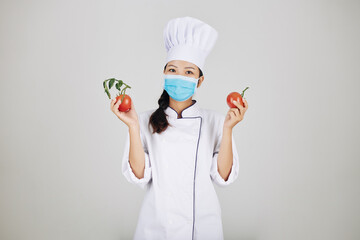 Positive young female restaurant chef in medical mask holding fresh tomatoes for sauce