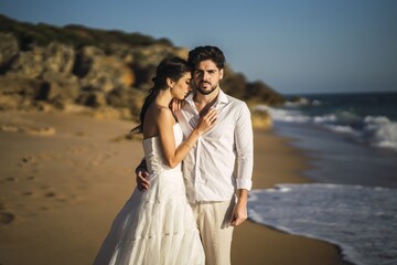 Sticker - Caucasian loving couple wearing white clothes and hugging in the beach during a wedding photoshoot