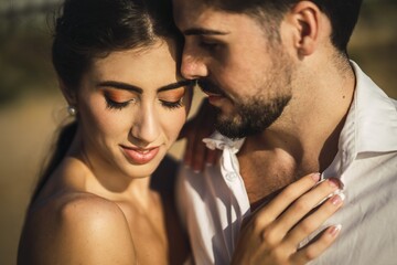 Wall Mural - Caucasian loving couple wearing white clothes and hugging in the beach during a wedding photoshoot