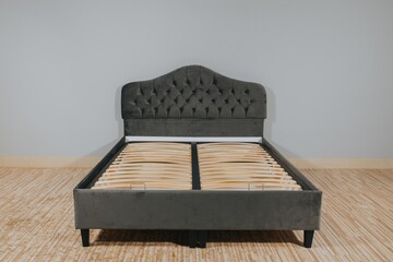 Sticker - Bed with gray fabric upholstery and a wooden frame without mattress in an empty room