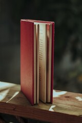 Poster - Vertical shot of a book with a red cover on a wooden fence in a garden under the sunlight