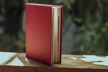 Poster - Closeup of a book with a red cover on a wooden fence in a garden under the sunlight