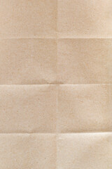 Close-up of the surface of wrapping craft paper with wrinkled lines and shadows. Empty texture sheet of cardboard from recycled material with a creases pattern, no waste concept. Beige background.