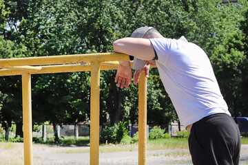 Young guy on the horizontal bar in nature in sunny, summer weather. Copy space - sport concept, quarantine, social distance, loneliness, healthy lifestyle, weight loss, fatigue