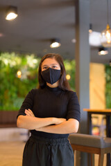 Young Asian businesswoman with arms crossed wearing mask and social distancing at the coffee shop