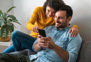 smiling young couple embracing while looking at mobile phone stock photo
