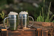 Wooden charred box. Two mugs with beer, white beer foam. Flame tanned wood. Blurred garden background.