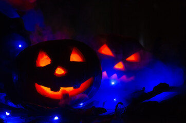 Two glowing pumpkins in the dark in the smoke in the forest close-up. One pumpkin peeks out from behind another. Beautiful background for Halloween.