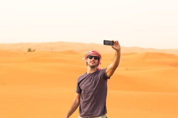 young male tourist taking a selfie with mobile phone camera in arab desert sand dunes during a safar