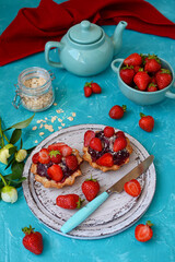 Wall Mural - Appetizing cake with strawberries, fresh ripe strawberries in a bowl and a teapot on a turquoise table. Vertical. The concept of a summer dessert.