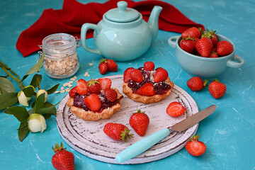 Wall Mural - Appetizing pastries with strawberries, fresh strawberries in a bowl, teapot on a turquoise table. The concept of a summer dessert.