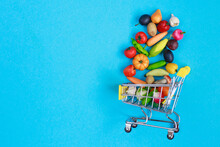 Metal Shopping Cart With Fruits And Vegetables On A Blue Background. Toy Miniature Shopping Trolley