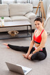 © Admiral - Portrait of young fitness woman with laptop, looking at camera, sitting on the floor in living room