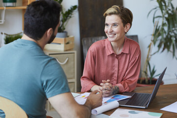 Portrait of modern young businesswoman speaking to colleague and smiling happily during meeting in office, copy space