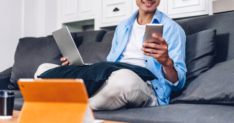 young smiling asian man relaxing using laptop computer working and video conference meeting at home.