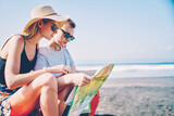 Fototapeta  - Romantic hipster couples holding map searching best route for driving during roadtrip on tropical island,male and female travelers thinking about navigation adventure during journey on summer weekends