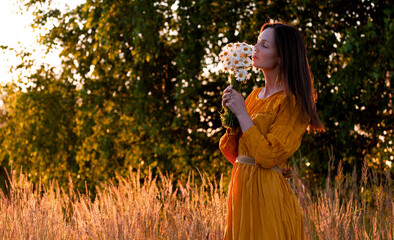 A 30-year-old woman in a Park in a long dress enjoys a bouquet of wild flowers. Youth, femininity, beauty, health.