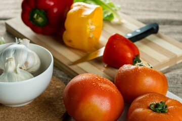 Wall Mural - Closeup shot of colorful peppers on a wooden cutting board tomatoes and garlic in the bowl