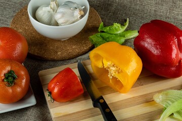 Wall Mural - Closeup shot of colorful peppers on a wooden cutting board tomatoes and garlic in the bowl