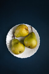 Over ripe green  delicious pear on a white plate against blue background. organic food concept
