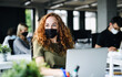 © Halfpoint - Young woman with face mask back at work in office after lockdown.