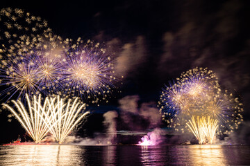 Holiday fireworks above water with reflection on the black sky background